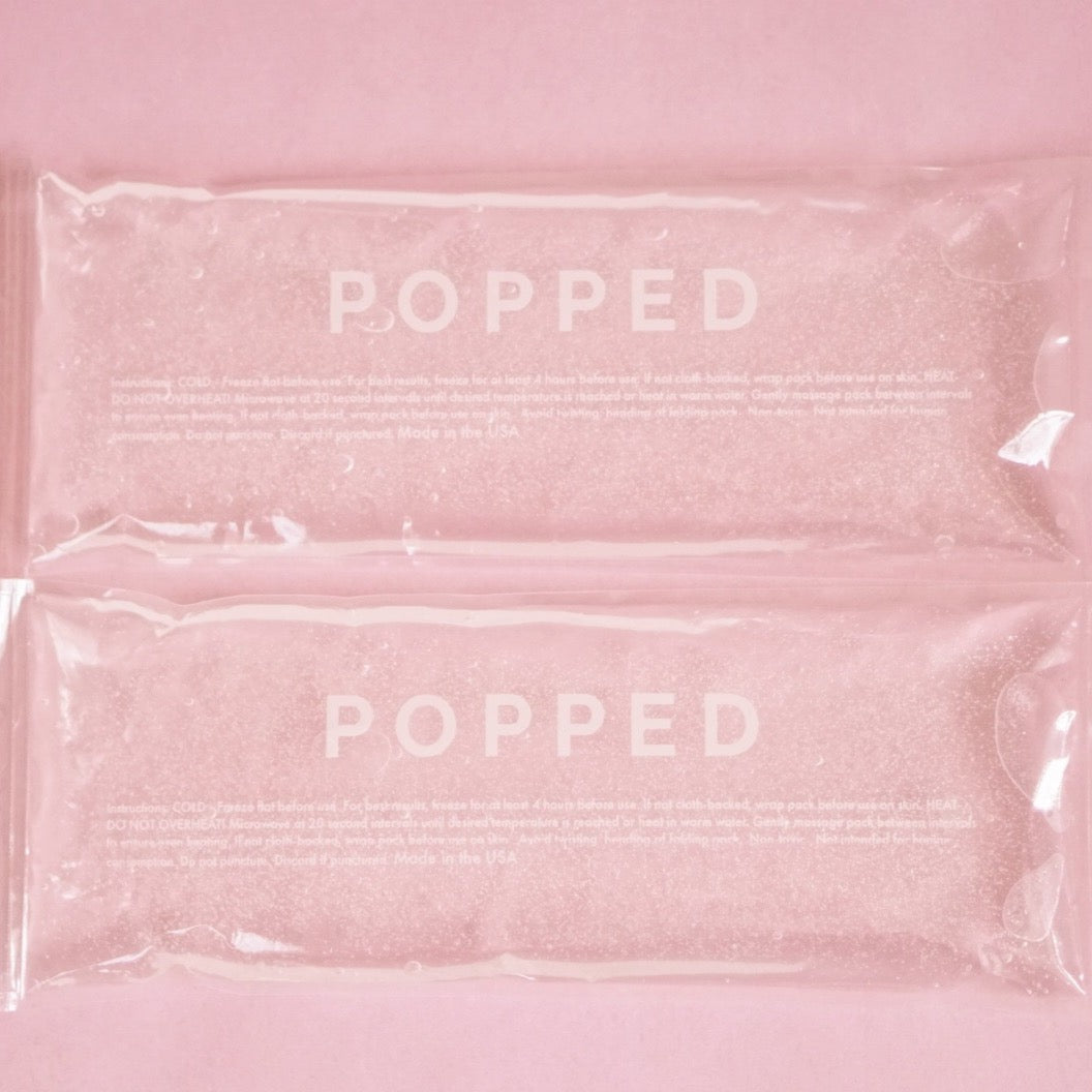 A two-count of hot and cold packs with clear, eco-friendly gel inside. They are both labeled with the brand name Popped, and they are on a pink background.
