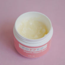 Load image into Gallery viewer, Jar of Organic Nipple Balm with no lid is shown from an angled top-down view so the label is visible. The balm appear smooth and light yellow.
