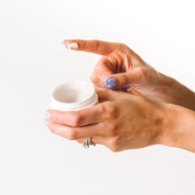 Load image into Gallery viewer, A woman&#39;s left hand holds the Popped Organic Nipple Balm jar while her right hand has some of the balm on its index finger for display.
