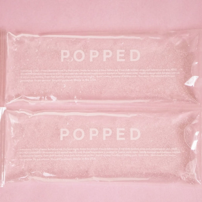 A two-count of hot and cold packs with clear, eco-friendly gel inside. They are both labeled with the brand name Popped, and they are on a pink background.